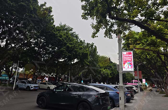 Outdoor pole LED banner displaying event information and advertisements near a sports venue entrance.