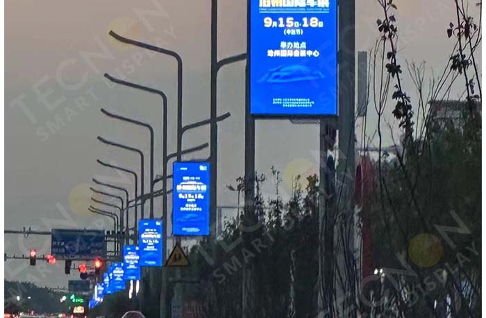 Brightly illuminated pole LED banners mounted on lampposts along the road, creating a dynamic nighttime advertising display.